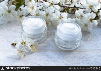 White can, cosmetic cream and cherry flowers on a white background. Face cream. White can, cosmetic cream and cherry flowers on a white background.