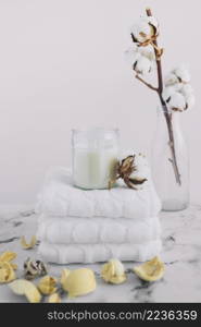 white candle candleholder stacked white napkins near dry pods cotton twig bottle