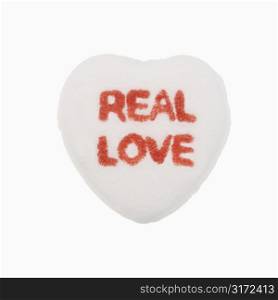 White candy heart that reads real love against white background.