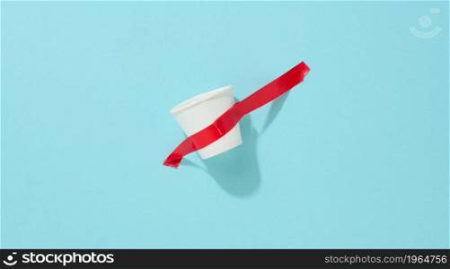 white cardboard cup glued with red sticky tape to the blue background