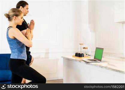 White caucasian fit sporty couple doing yoga tree pose in living room at home watching online tutorials from trainer on laptop. Working out, fitness sport and healthy lifestyle concept.