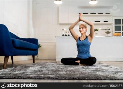 White caucasian fit sporty woman doing yoga Sukhasana sit pose in living room at home for mental health and meditation. Working out, fitness sport and healthy lifestyle concept.