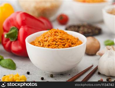 White ceramic bowl plate with boiled red long grain basmati rice with vegetables on light background with sticks and paprika pepper with corn,garlic and basil.