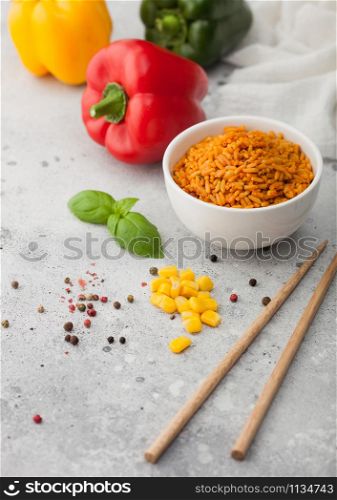White ceramic bowl plate with boiled red long grain basmati rice with vegetables on light background with sticks and paprika pepper with corn,garlic and basil.