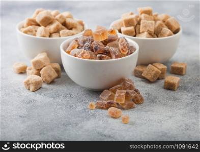 White ceramic bowl plates of natural brown unrefined and caramelized sugar cubes on light background.