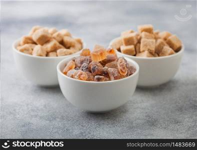 White ceramic bowl plates of natural brown unrefined and caramelized sugar cubes on light background.