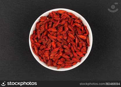 white ceramic bowl with goji berries on dark stone background