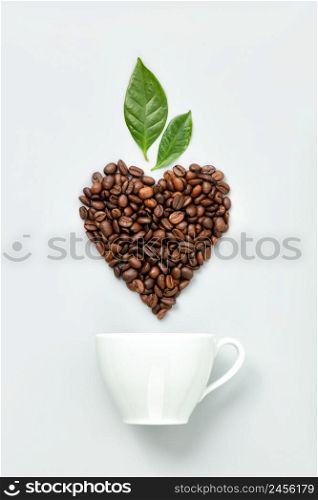 White ceramic coffee cup and coffee beans in shape of heart on white background, flat lay