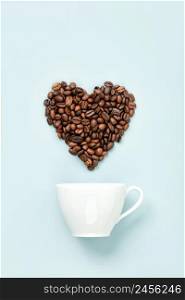 White ceramic coffee cup and coffee beans in shape of heart on blue background, flat lay