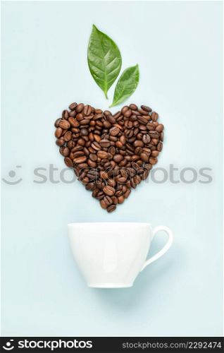 White ceramic coffee cup and coffee leaves and beans in shape of heart on blue background, flat lay