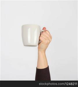 white ceramic cup in a female hand on a white background, hand is raised up