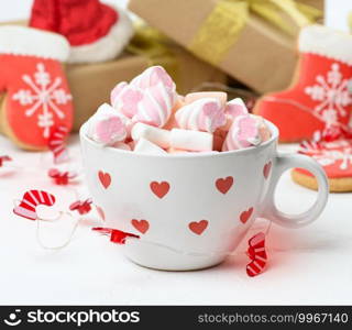 white ceramic cup with cocoa and marshmallows, behind a gift box and a Christmas toy, close up