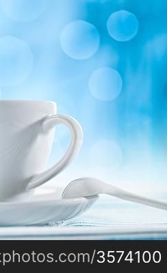 white ceramic cup with spoon on blurry blue background