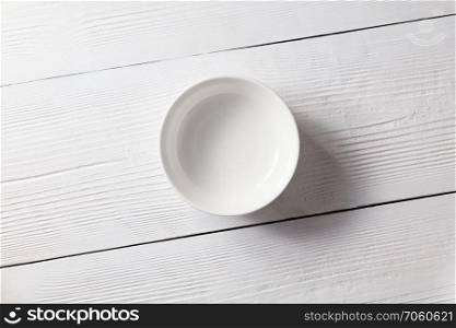 White ceramic empty plate on a white wooden table with copy space.. One empty plate on a white wooden kitchen table. Top view