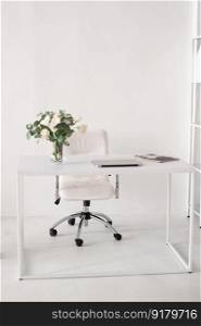 white chair, leather chair, workplace, laptop, vase with flowers, table with objects, office, collaboration, marketing, advertising, place for text. Office environment. A white room with a desk on which there is a vase, a laptop and magazines