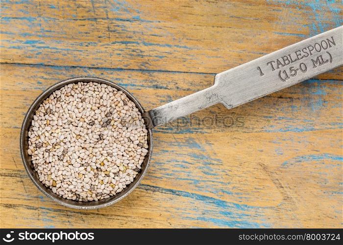 white chia seeds (Salvia Hispanica) in a measuring tablesoon against grunge painted wood