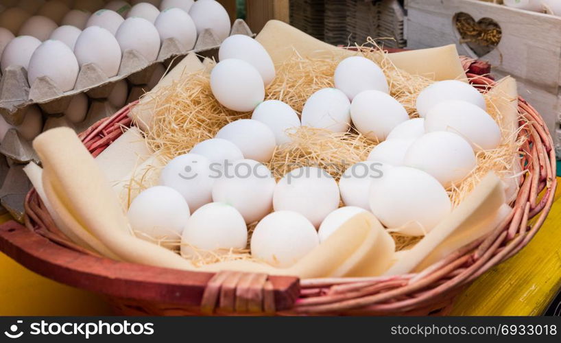 White chicken eggs leaning on straw in wooden basket at market,outdoor.