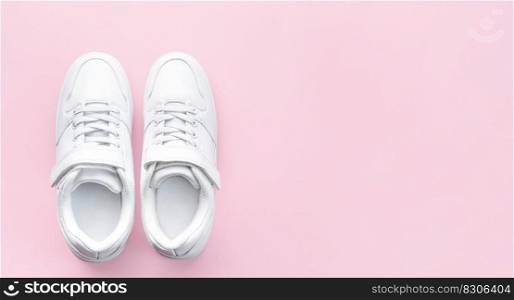 White children’s sneakers on a pink background with copy space. Banner.