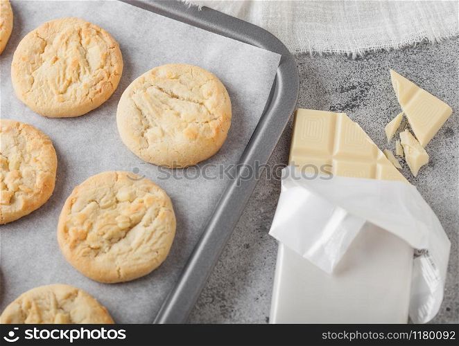 White chocolate biscuit cookies on baking tray on light kitchen table background with white chocolate bar. Top view