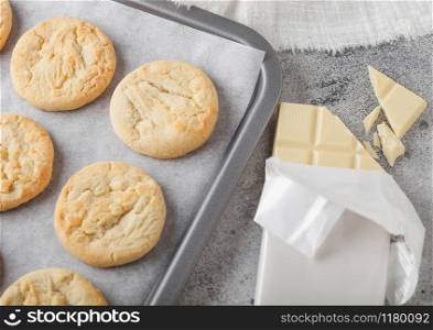 White chocolate biscuit cookies on baking tray on light kitchen table background with white chocolate bar. Top view