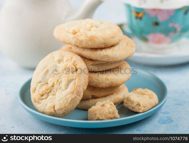 White chocolate biscuit cookies on blue ceramic plate with tea pot and cup on blue table background.