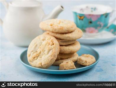 White chocolate biscuit cookies on blue ceramic plate with tea pot and cup on blue table background.