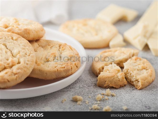 White chocolate biscuit cookies on white ceramic plate with chocolate blocks and curls on light table background.