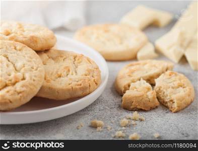 White chocolate biscuit cookies on white ceramic plate with chocolate blocks and curls on light table background.