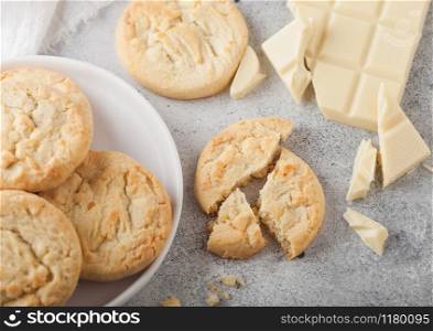White chocolate biscuit cookies on white ceramic plate with chocolate blocks and curls on light table background. Top view