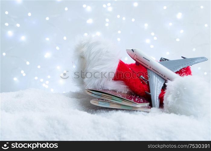 White christmas background with fresh snow and lights. Christmas red hat, plane and passports. Holiday travel and vacations concept.. White christmas with snow