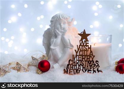 White christmas - burning advent candle and cute angel in snow , blue night with lights in background. Happy Christas and holidays concept.. White christmas with snow