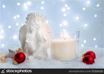 White christmas - burning advent candle and cute angel in snow , blue night with lights in background. White christmas with snow