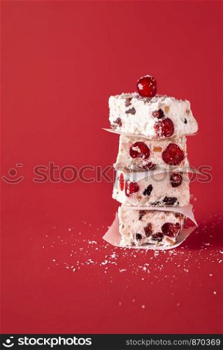 White Christmas cookies piled in a stack, homemade with coconut and glace cherries, on a red background. Traditional Australian Xmas dessert.