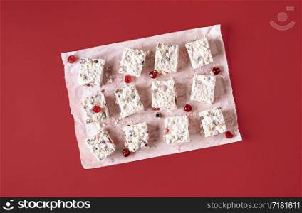 White Christmas dessert cut in pieces on baking paper on a red background. Above view of Australian food. Flat lay of dried fruits and coconut cake.