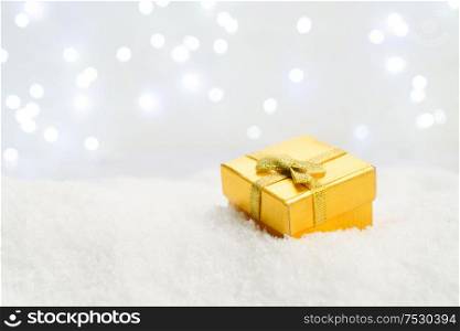 White christmas. - golden gift box in snow, lights in background. White christmas with snow