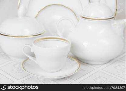 White classic crockery for tea: teapot, cup, serving plate and sugar bowl on a beautiful tablecloths