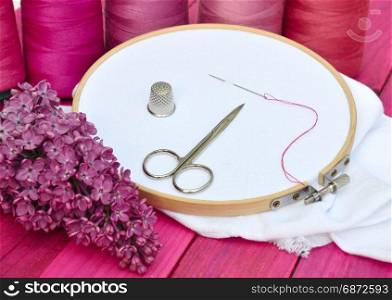 white cloth in wooden embroidered embroidery frame, behind a row of thread reels in red