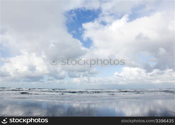 white clouds and blue sky reflected in wet beach