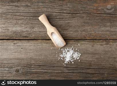 white coarse salt in a wooden spoon, gray table from old boards, top view