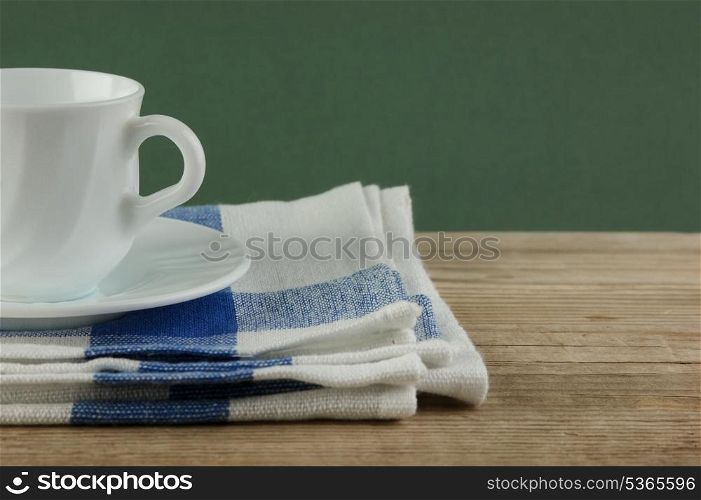 White coffee cup and dishcloth on old wooden table over green background