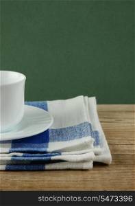 White coffee cup and dishcloth on old wooden table over green background