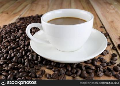 White coffee cup and roasted coffee beans on wood background.