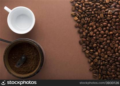 White coffee cup, coffee grinder and coffee beans on brown background. Top view. Focus on grinder