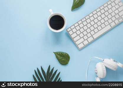 white coffee cup headphone keyboard with leaves blue backdrop