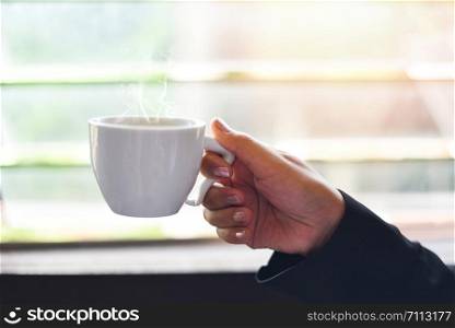 White coffee cup in hand , close up / Business woman holding coffee cup by the window with sunlight in the morning