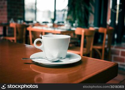 White coffee cup on wooden table in coffee shop blur background. White coffee cup on wooden table in coffee shop blur interior background, vintage style photo