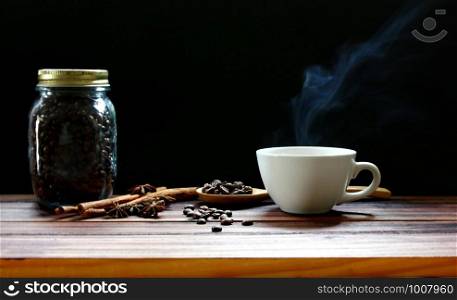 white coffee cup with hot steam shape. coffee mug with roasted coffee beans, cinnamon, star anise on wood table isolate on black background.