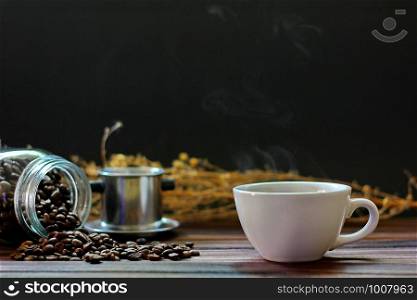 white coffee cup with hot steam shape. coffee mug with roasted coffee beans, cinnamon, star anise on wood table isolate on black background.
