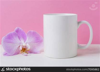 White coffee mug mockup on the pink background with purple orchid. Empty mug mock up for design promotion.
