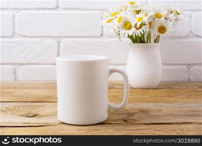 White coffee mug mockup with chamomile bouquet in rustic vase. White coffee mug mockup with white field chamomile bouquet in handmade rustic vase. Empty mug mock up for design promotion.